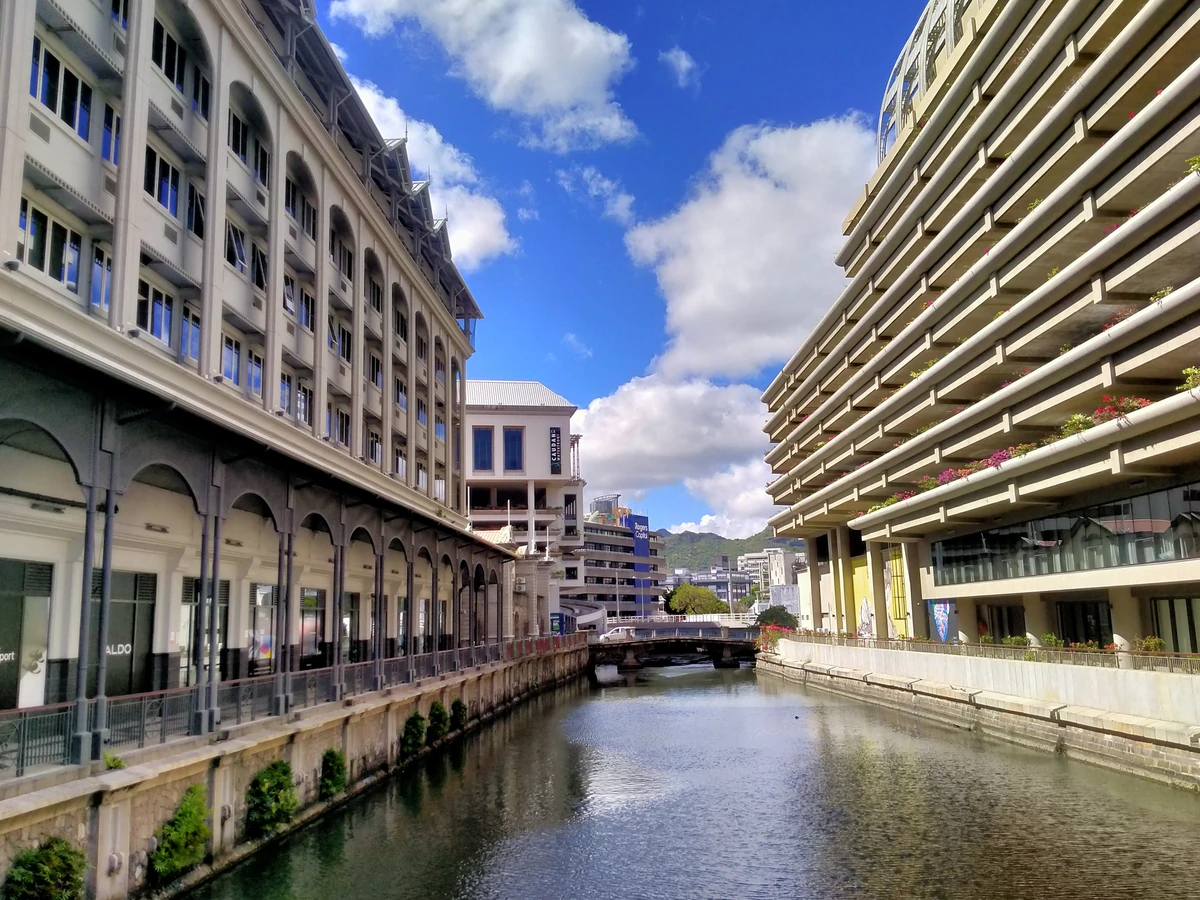 Canal at Caudan Waterfront in Port Louis, linked to Ruisseau du Pouce, with water flowing between waterfront buildings toward the harbour.