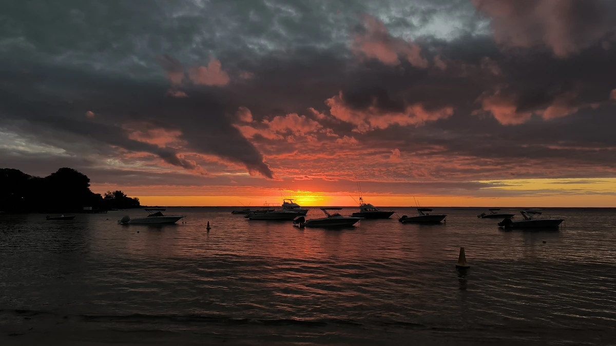 Silhouettes of pirogues at sunset on Albion public beach, with dramatic clouds and orange light on the horizon.