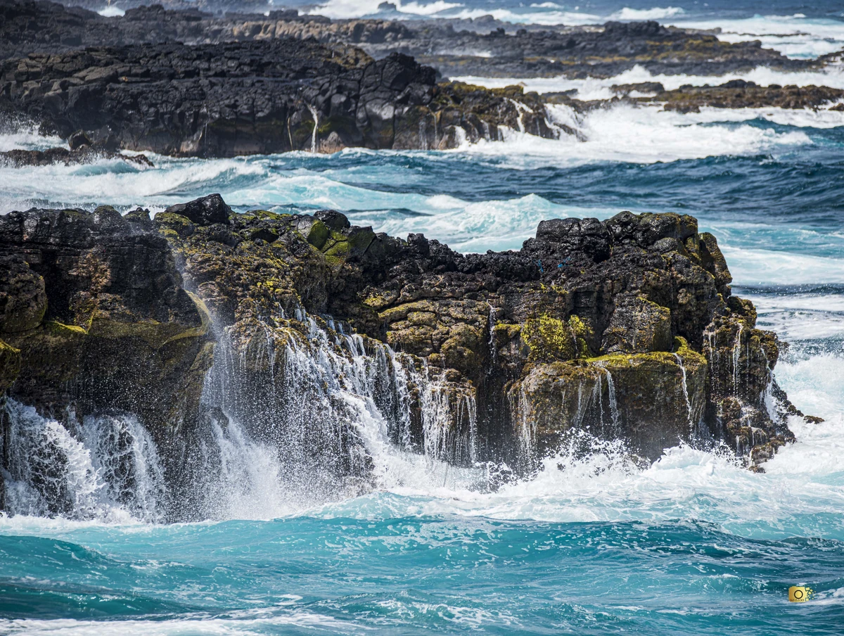Seawater flowing down black volcanic rocks at Pont Naturel after a wave, with turquoise water and rough sea on the south-east coast of Mauritius.