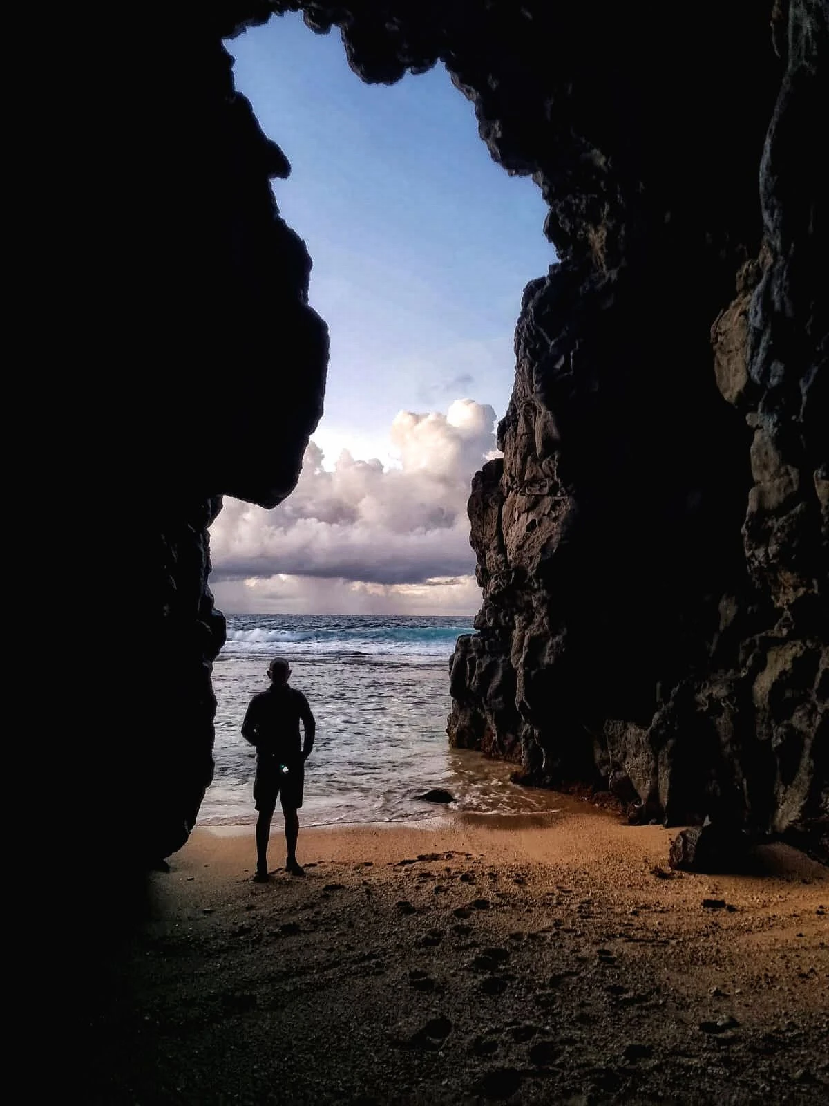 Man standing inside Gris Gris cave in Souillac, Mauritius, looking out at the rough ocean and rocky south coast.