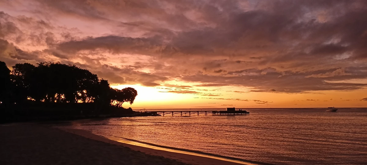 Sunset behind the Club Med jetty in Albion, with calm sea, colourful clouds, and the beach in silhouette.
