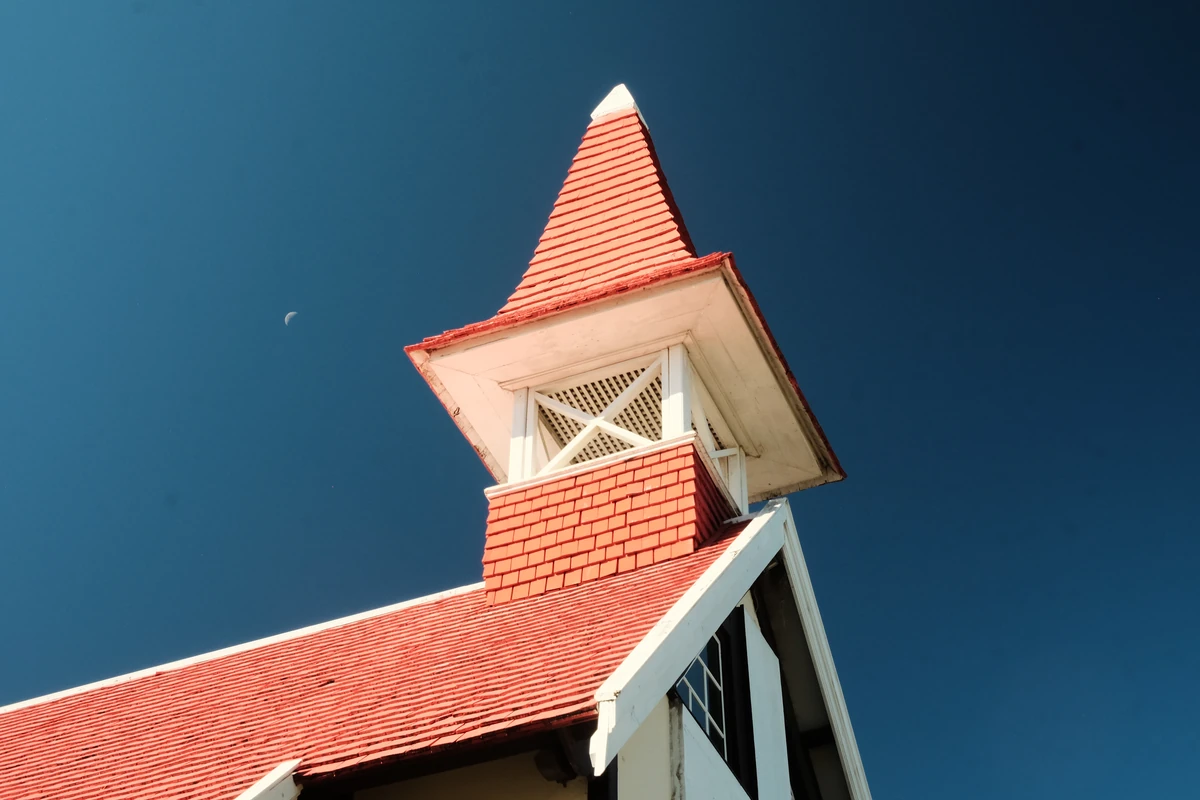 Top part of the red-roofed church at Cap Malheureux with white wooden details, blue sky, and a small crescent moon.