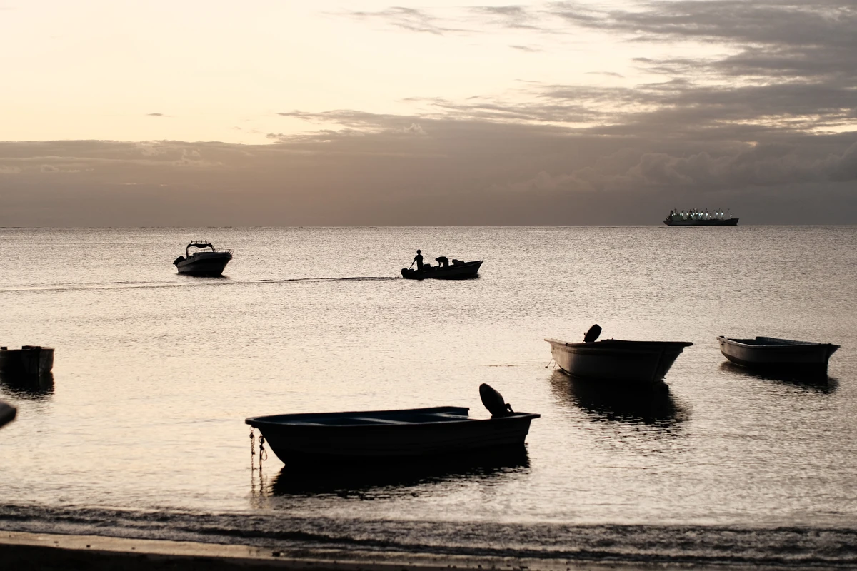 Silhouetted boats floating on calm water after sunset at Bain des Dames beach.