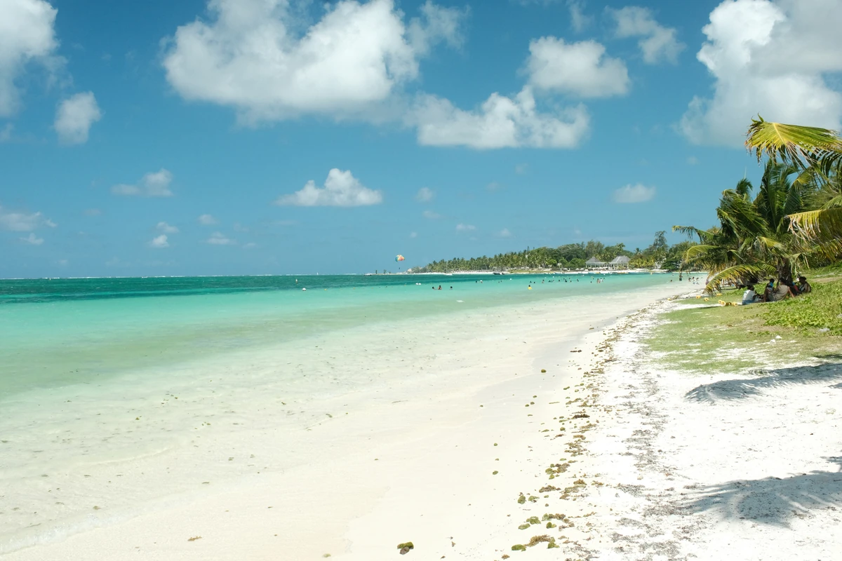 Bright sunny day on Belle Mare beach with white sand, turquoise lagoon water, coconut palms, and blue sky.