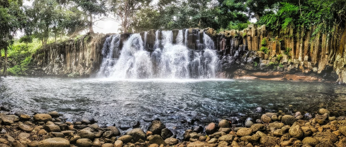 Panoramic view of Rochester Falls near Souillac, Mauritius, showing water flowing over dark basalt columns into a natural pool.