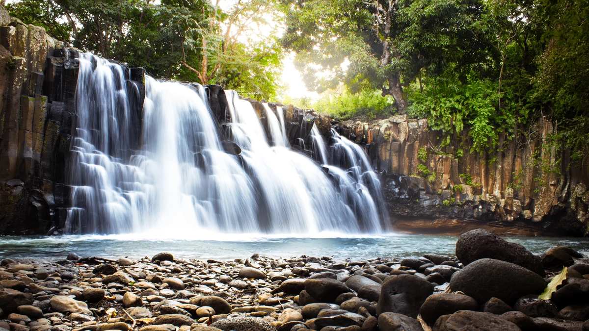 Long-exposure photo of Rochester Falls near Souillac, Mauritius, showing silky water flowing over basalt columns into a natural pool.