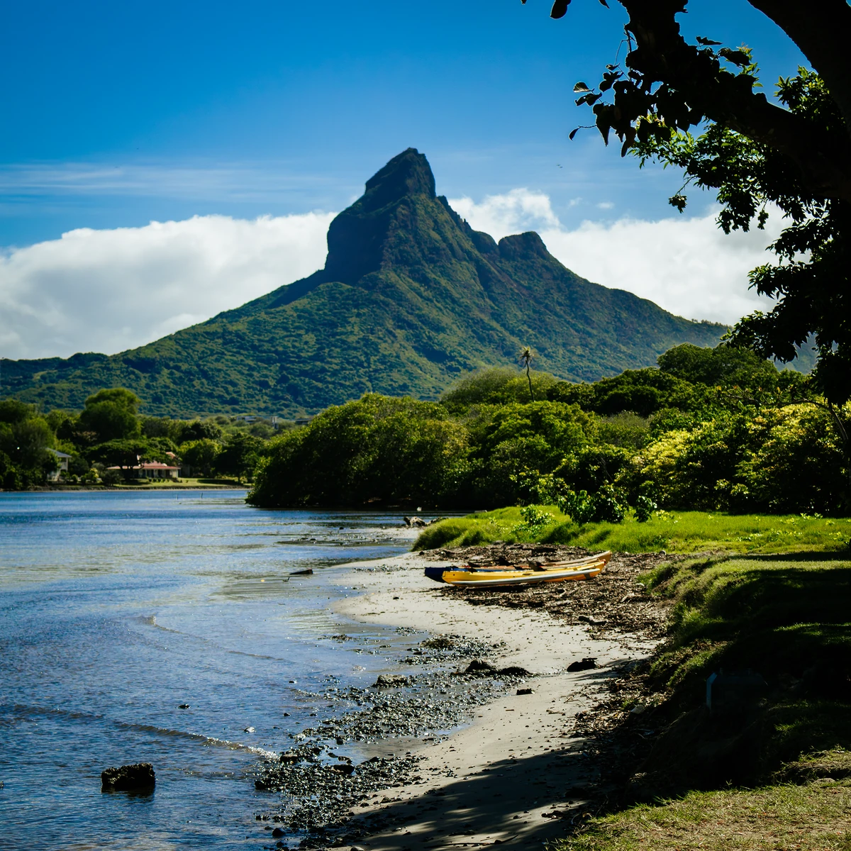 View of Rempart Mountain from Tamarin river mouth, with calm water, shoreline, greenery, and a small boat.