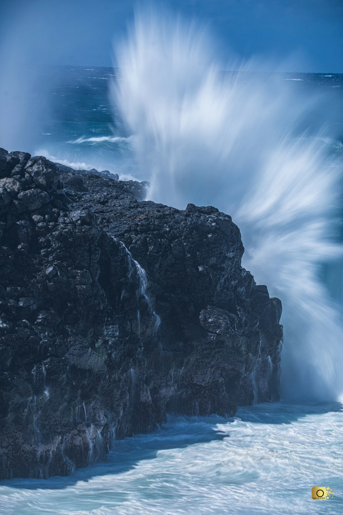 Powerful waves crashing against dark volcanic cliffs at Le Souffleur in Mauritius, creating high sea spray above the rocky coast.