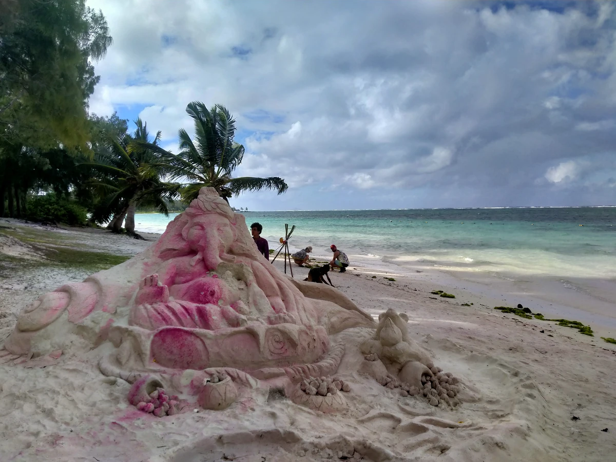 Ganesh idol sculpted from sand on Belle Mare Beach in Mauritius, with the turquoise lagoon and coconut palms in the background.