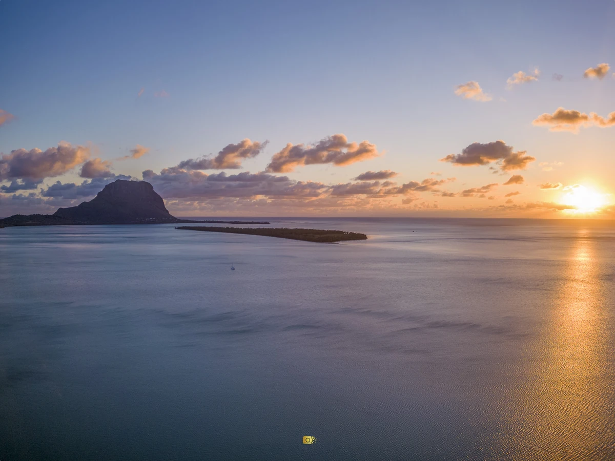 Aerial drone view of Île aux Bénitiers at sunset with Le Morne Brabant, lagoon, reef line and golden evening light on the south-west coast of Mauritius.