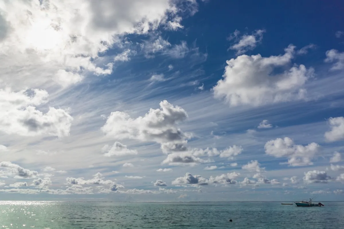 Windy white clouds above calm ocean with fishing boat at Le Paradis Beachcomber, Mauritius