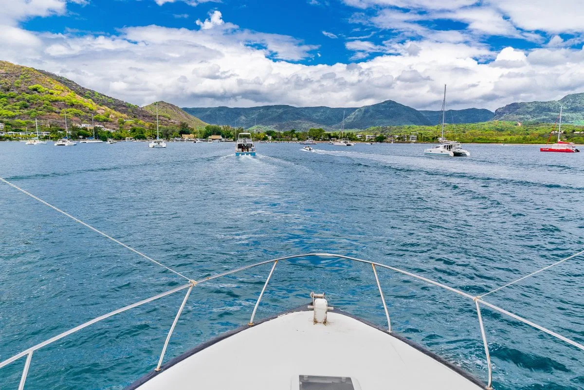 Fishing boats returning to Le Morne Anglers' Club in Mauritius with mountain views and cloudy skies