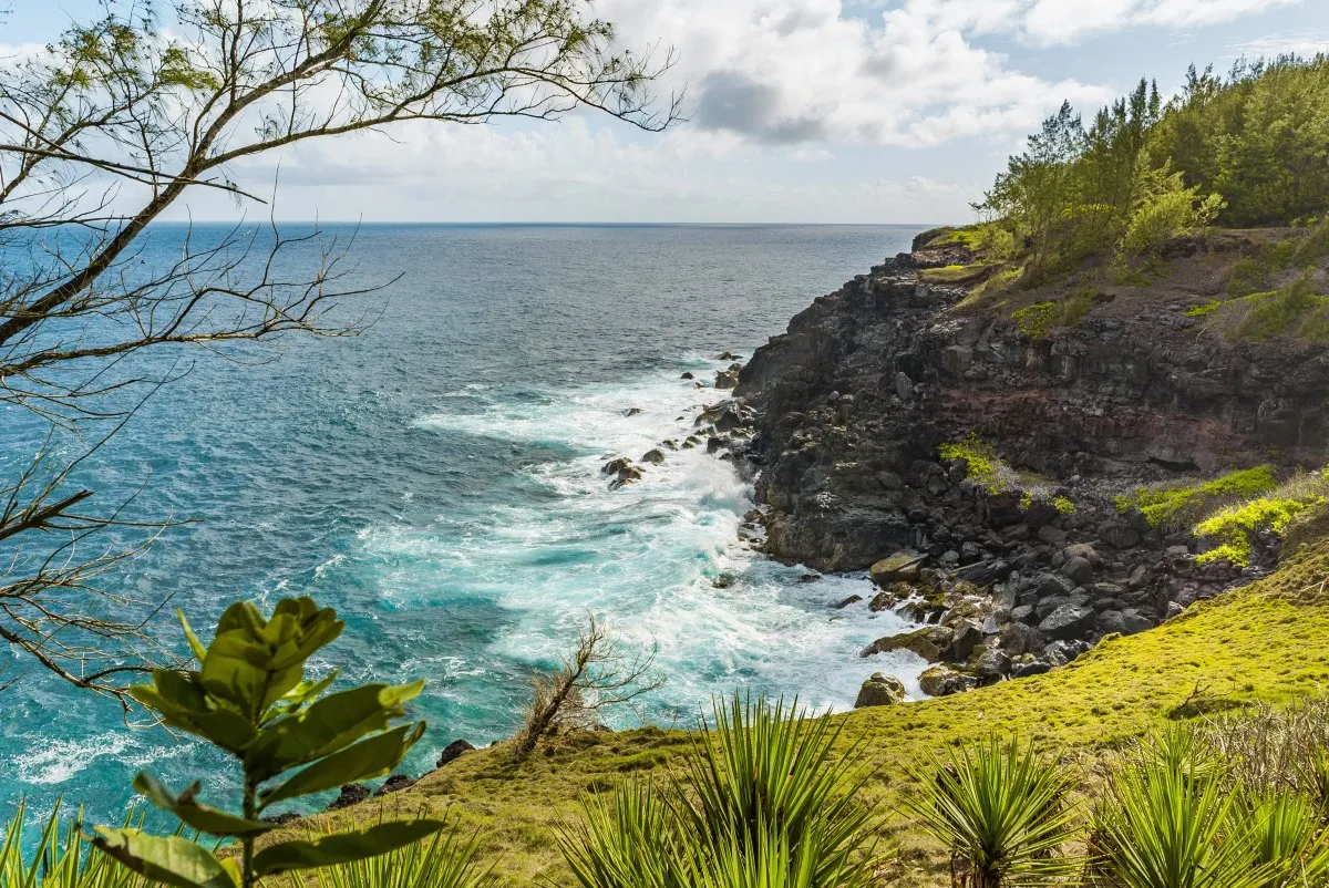 Rocky precipice slope with green grass and waves crashing near Andrea Lodges in Mauritius