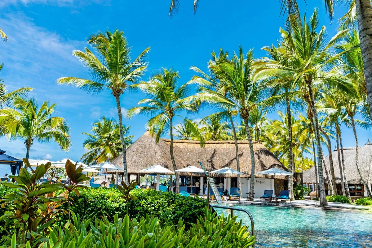 Hotel pool with palm trees and green plants under a blue sky in Mauritius