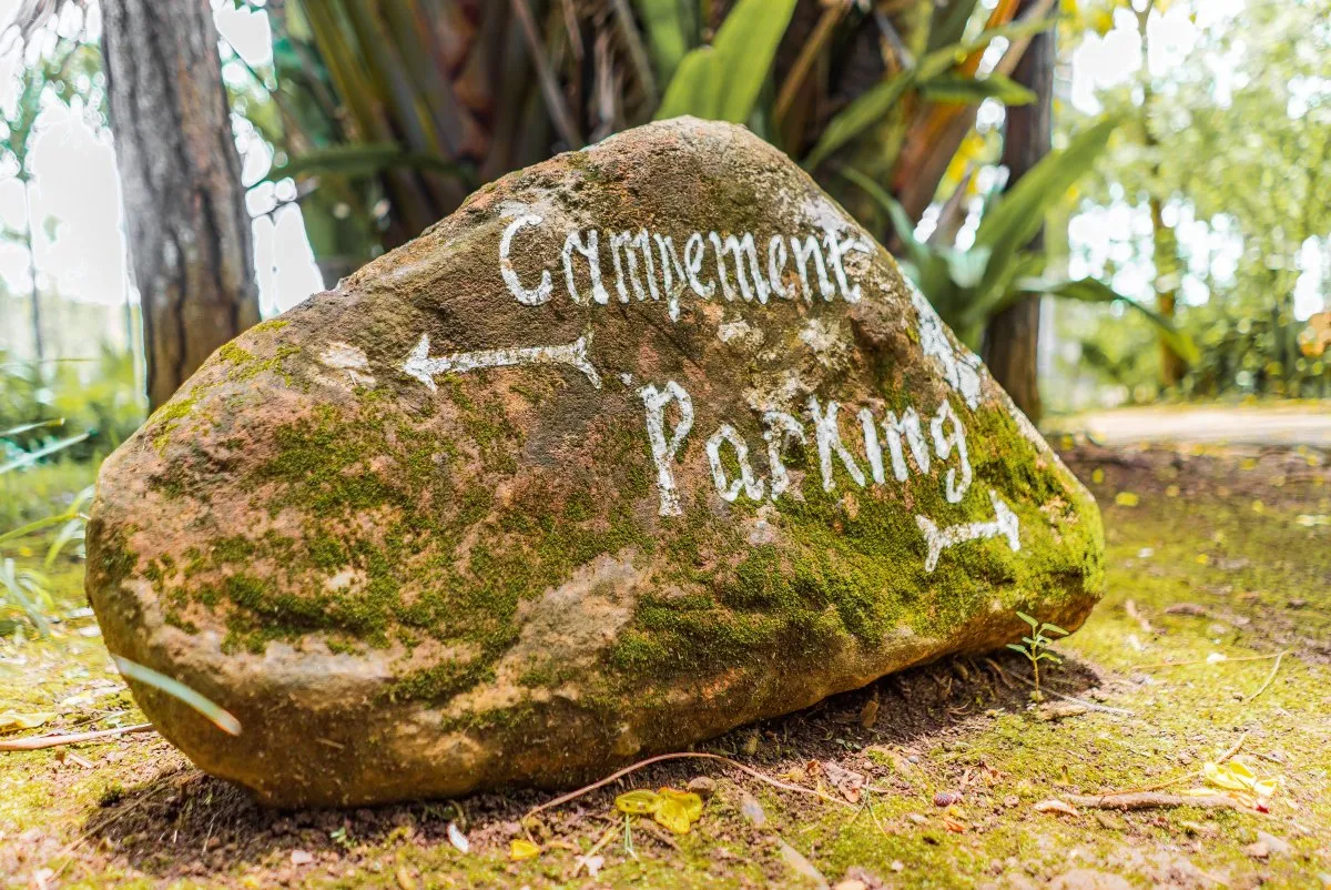 Natural rock signage with green moss at L'Exil Lodges in Mauritius indicating campsite and parking