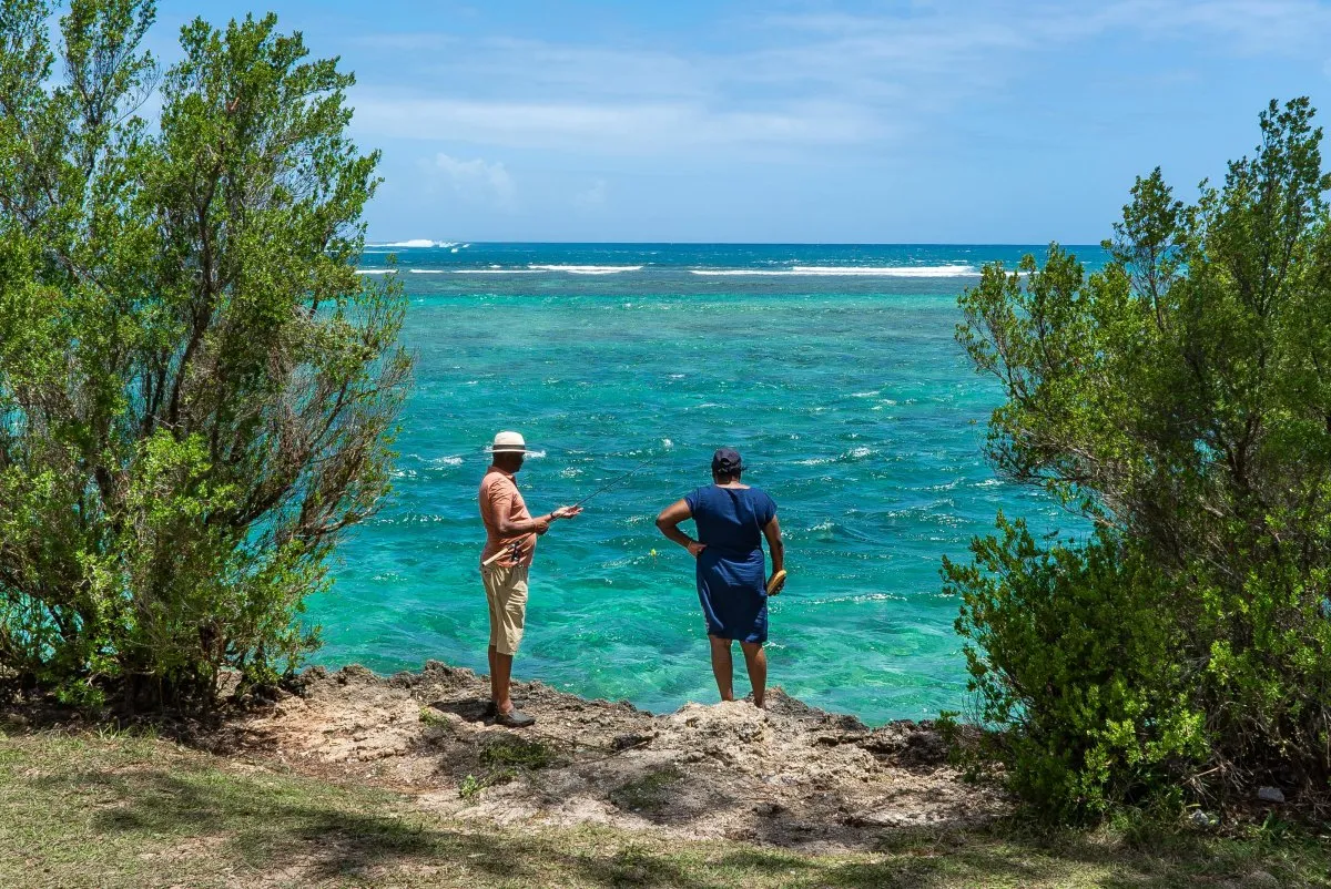 Fisherman fishing near volcanic rock formation at La Prairie, Mauritius with bushes around