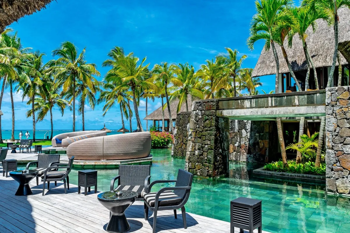 Sunny view of Constance Belle-Mare Plage hotel restaurant and pool with coconut trees and lagoon in Mauritius