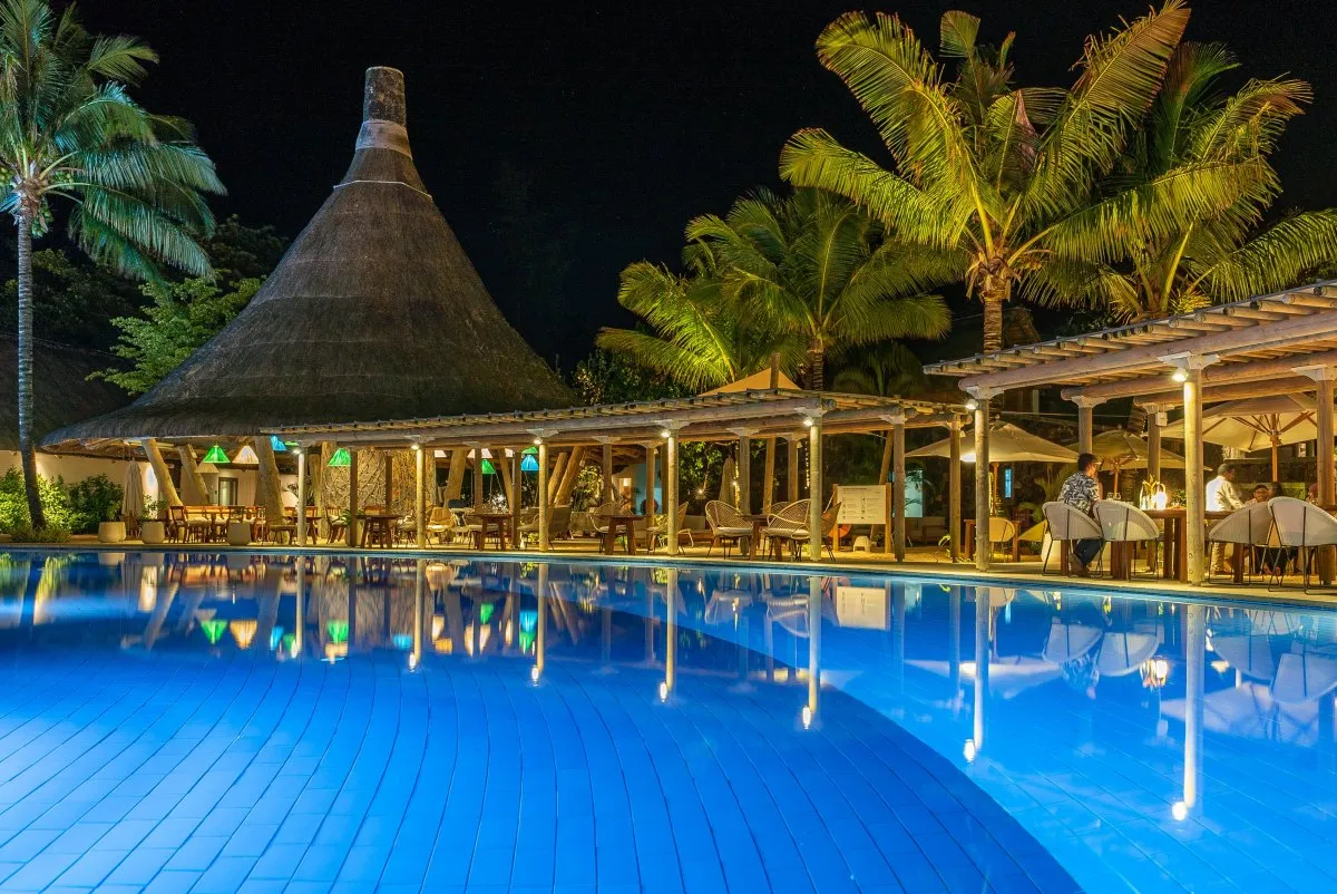 Illuminated pool reflecting lights at C Beach Club restaurant with palm trees in Mauritius at night