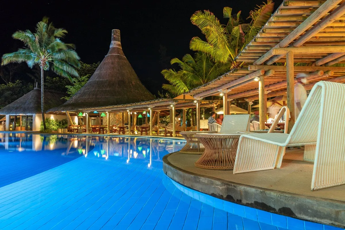Illuminated blue pool and cozy seating area at C Beach Club in Mauritius at night