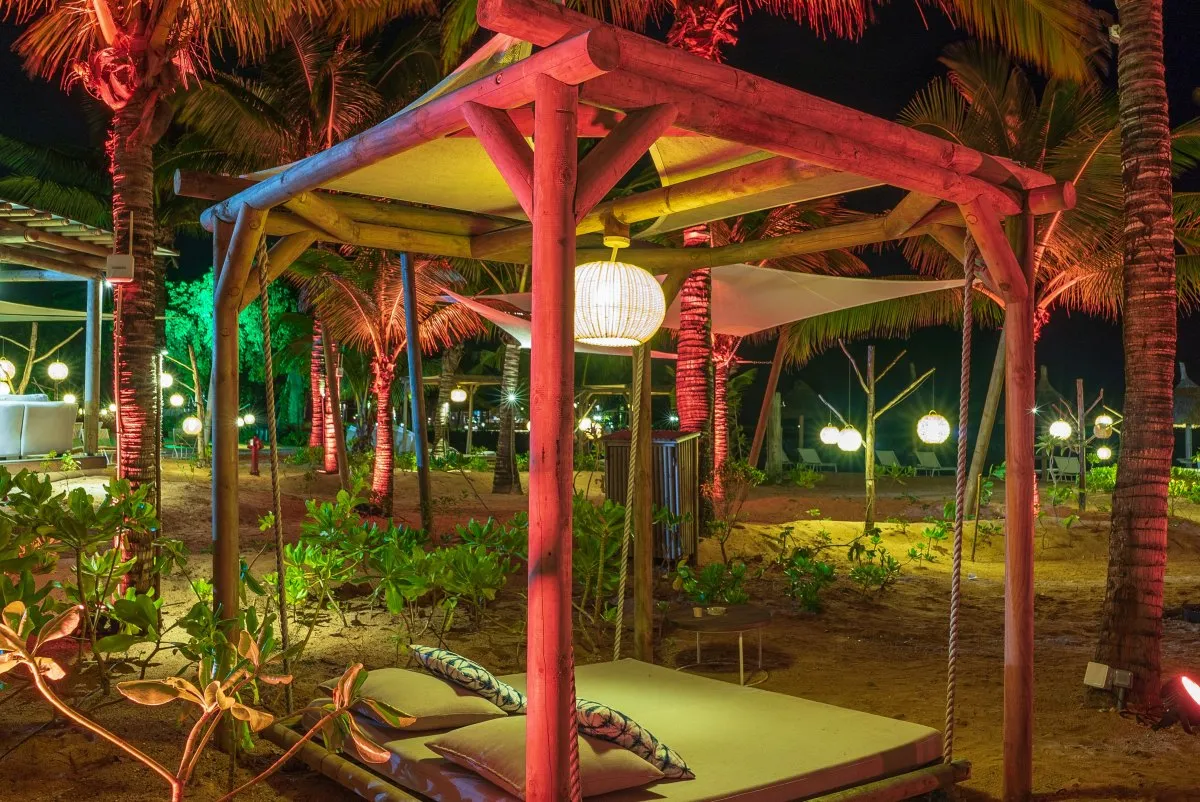 Outdoor wooden canopy relaxing bed lit up at night in C Beach Club sand garden, Mauritius surrounded by plants