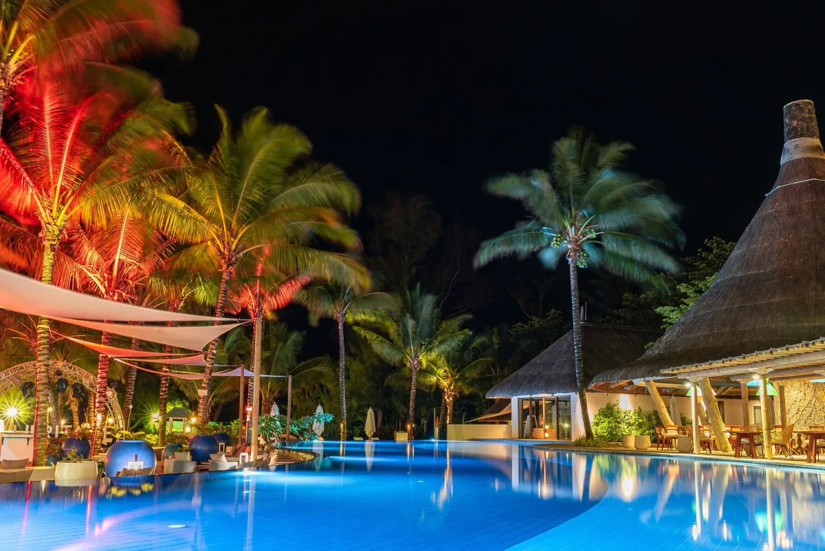 Blue infinity pool at Heritage C Beach Club in Mauritius surrounded by coconut trees at night