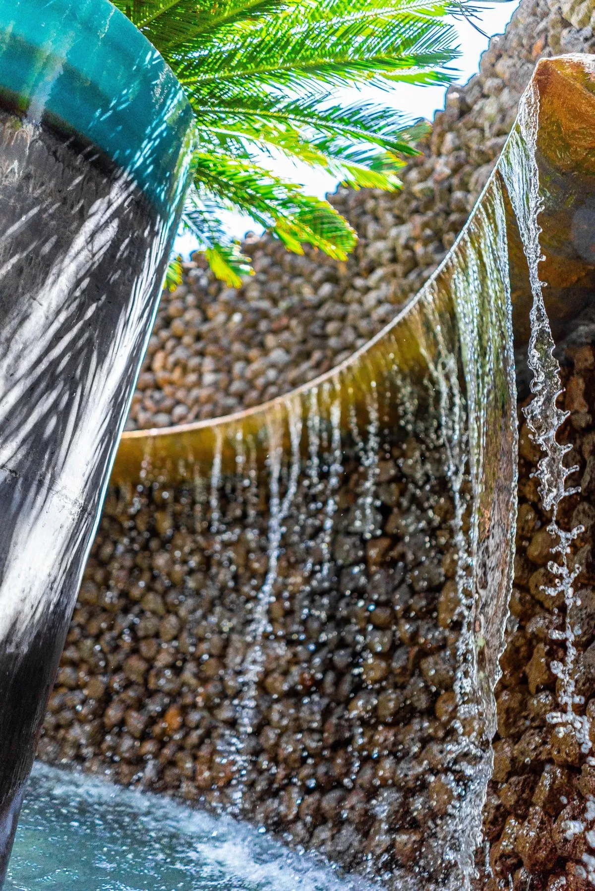 Decorative cascade with flowing water on brown rocks by a pond and sago palm at Constance Belle-Mare Plage Hotel, Mauritius