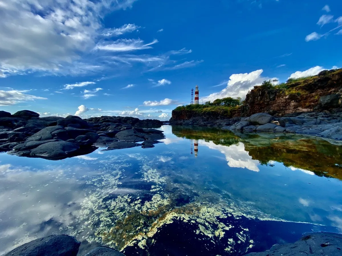 Reflection of Albion Lighthouse on calm water in Mauritius with nearby cliffs
