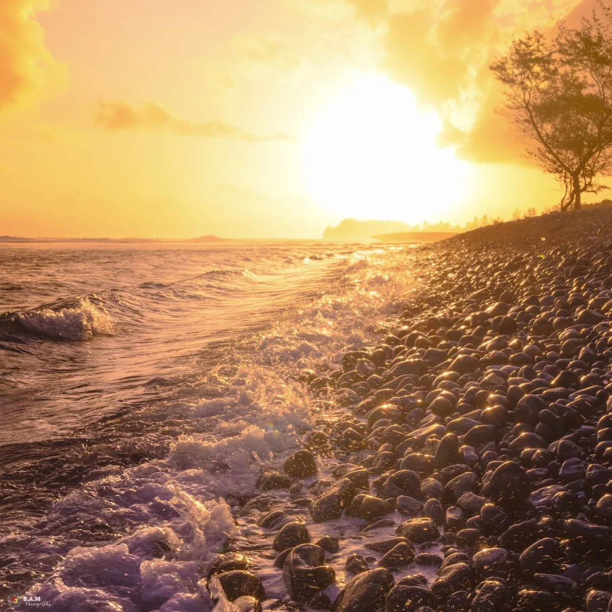 Sunrise over Rivière des Galets rocky beach with waves and black pebbles in Mauritius