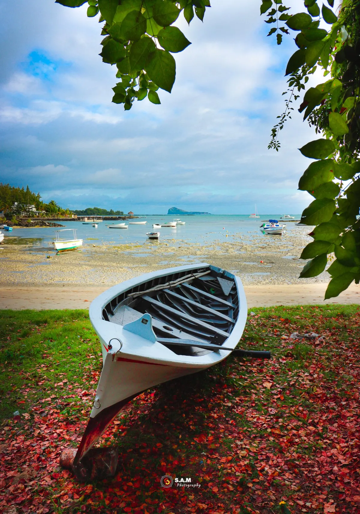 White pirogue boat on grassy beach at Grand Gaube in Mauritius surrounded by dry brown leaves
