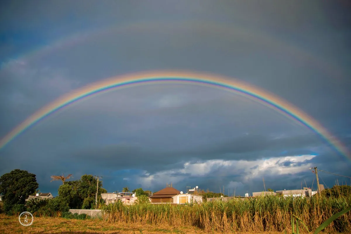 Double rainbow arching over sugarcane fields in Mauritius under a cloudy sky