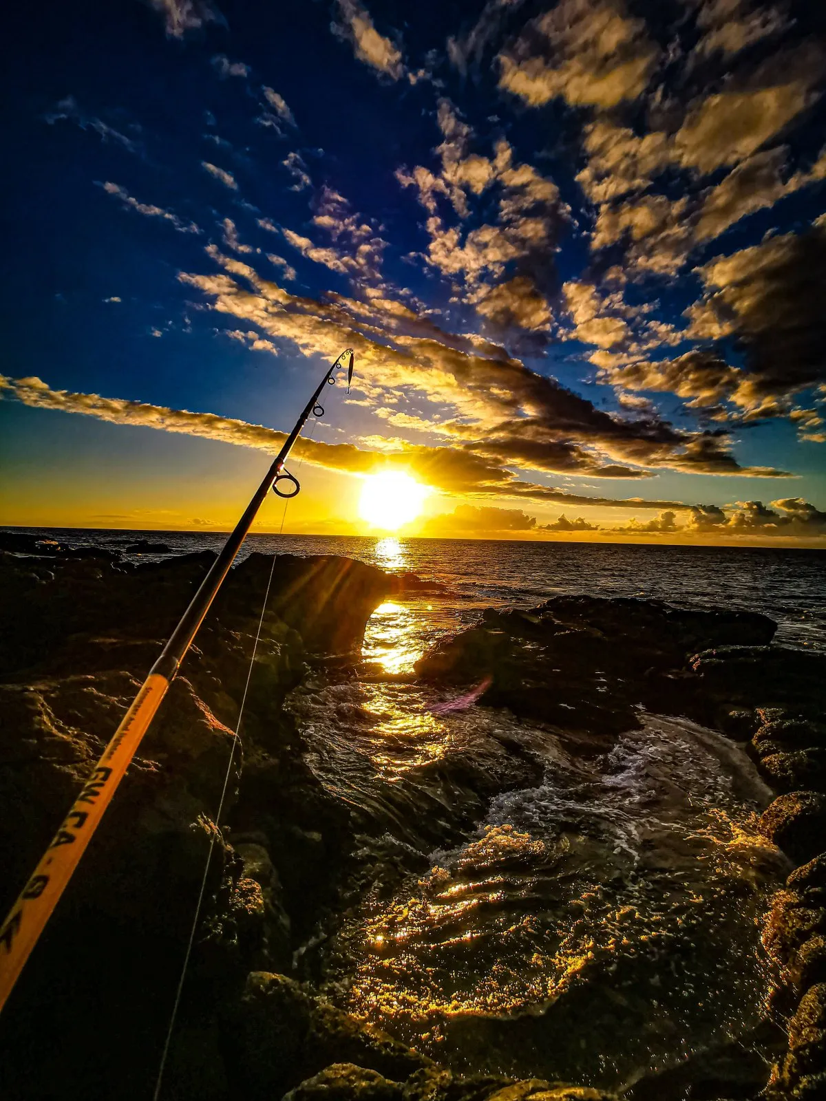 Fishing on rocky shore at sunset with waves in Flic en Flac, Mauritius.