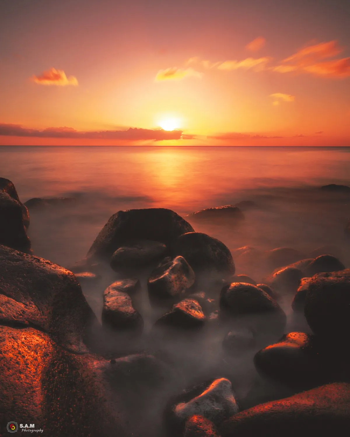 Long exposure photo of rocky shore reflecting orange sunset light on the sea in Mauritius