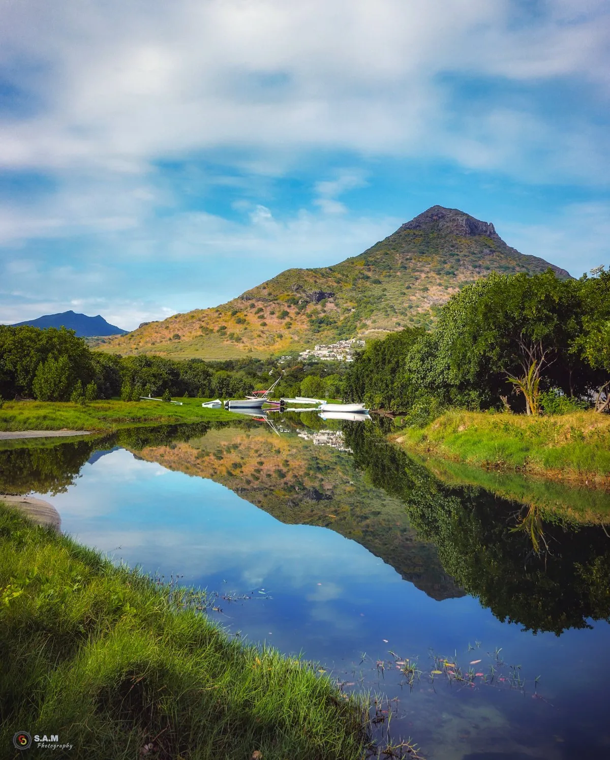Reflection of La Tourelle Mountain and clouds in a river with boats and trees in Tamarin, Mauritius