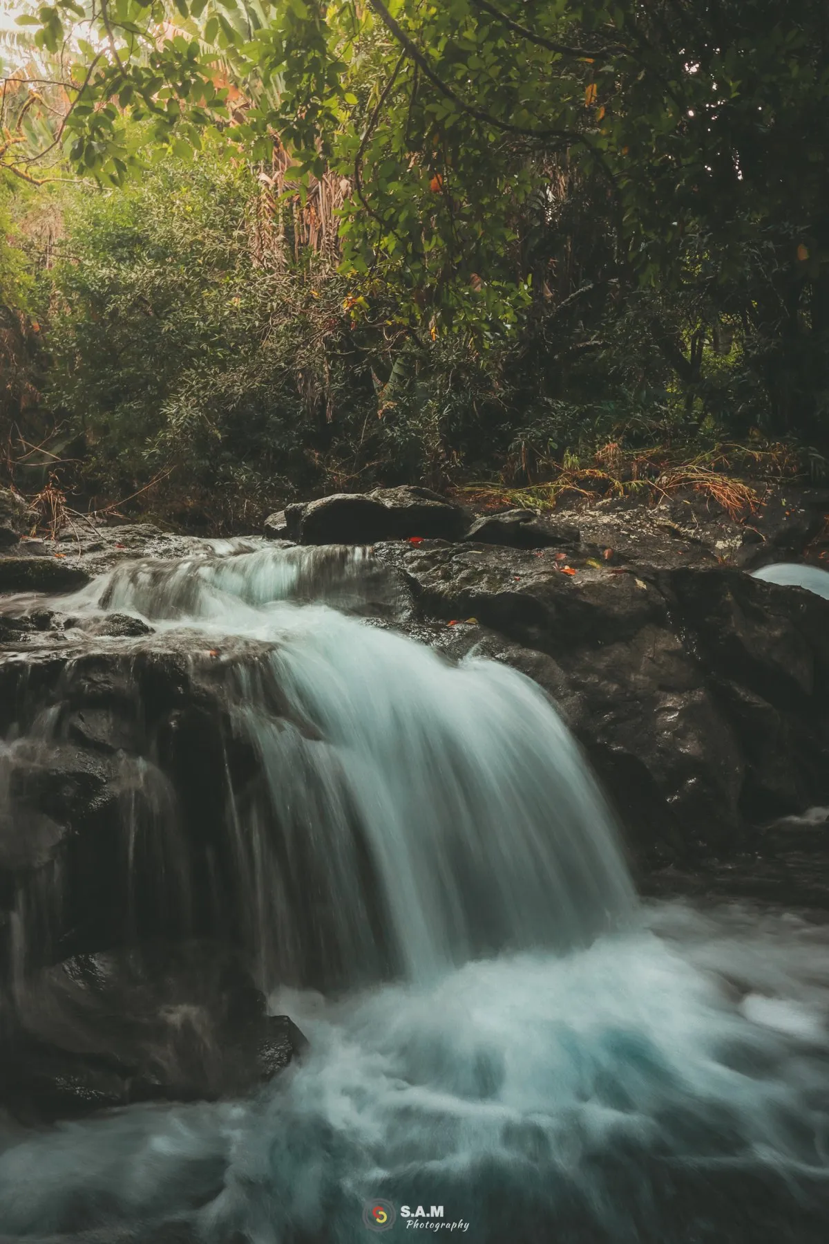 Long exposure photo of Eau Bleu waterfall cascading over black rocks in a lush Mauritius forest