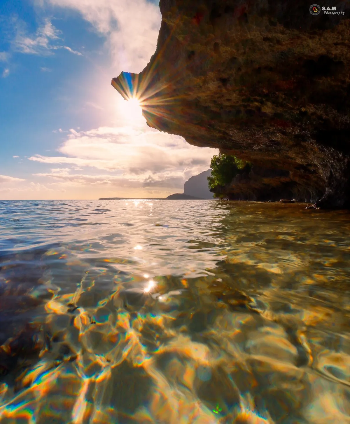 Sun rays shining under a coral rock formation in shallow water at La Prairie beach, Mauritius