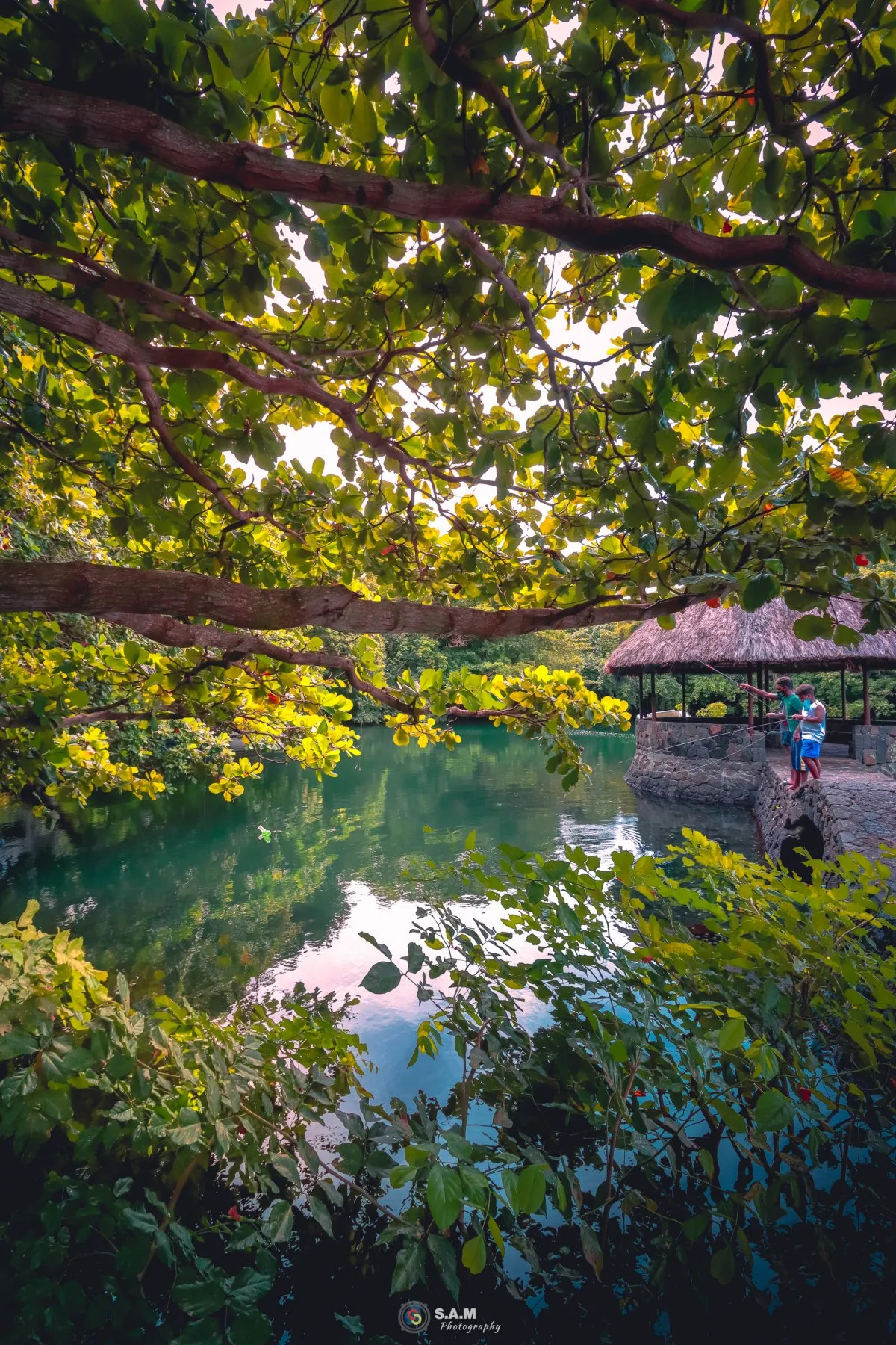 Two fishermen standing on a natural rock jetty with a straw roof at Trou d'Eau Douce, Mauritius