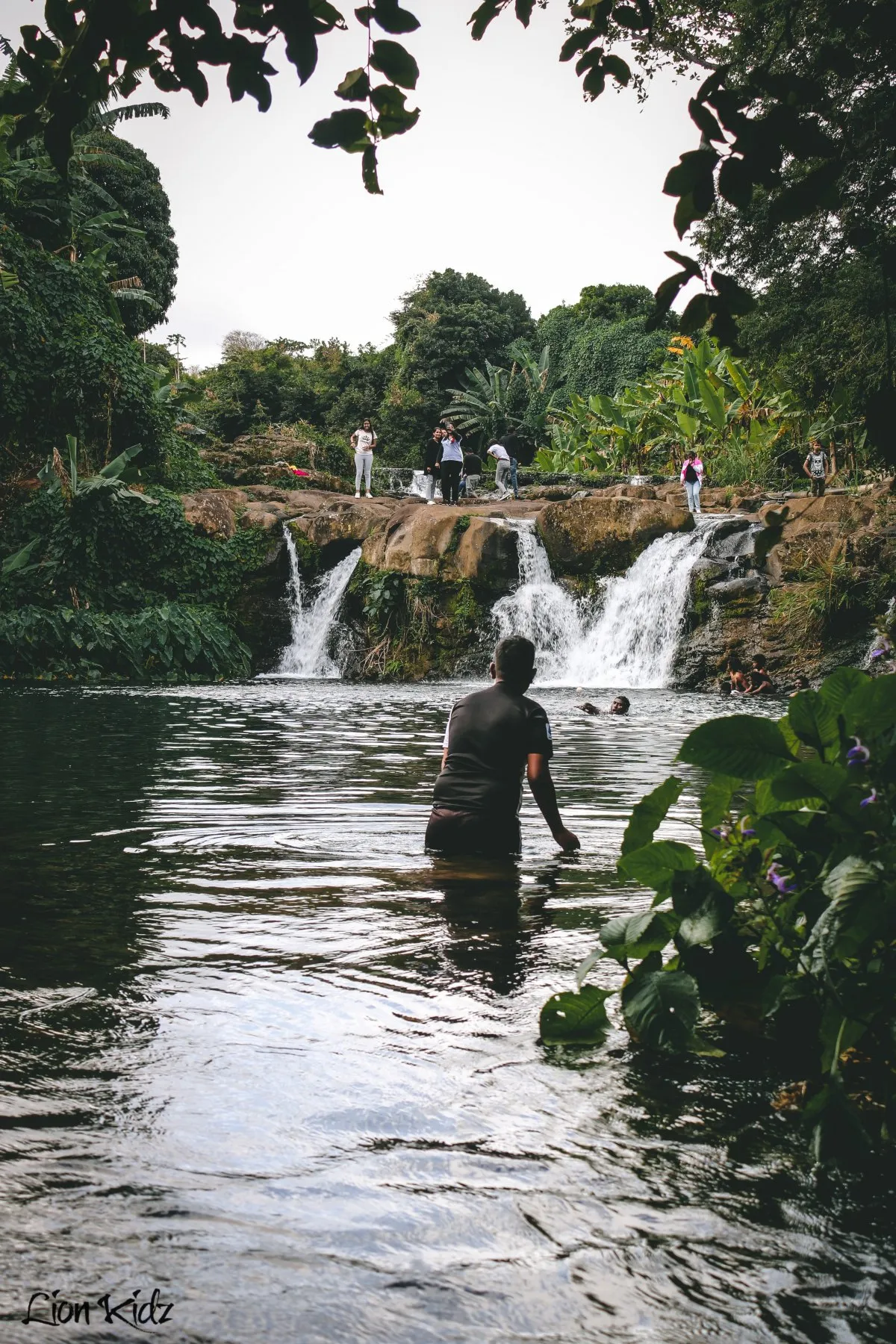 Men swimming near waterfalls at Marmite River in Mauritius surrounded by lush plants