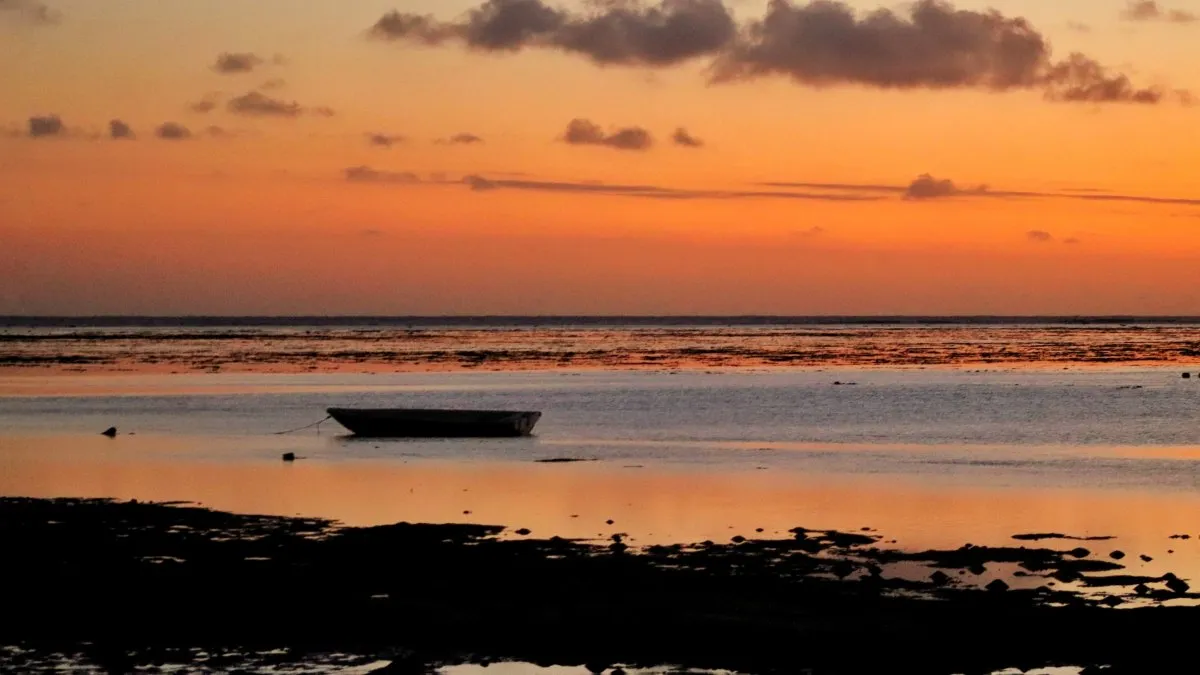 Golden hour sunset with boat silhouette over calm waters at La Prairie Beach, Mauritius