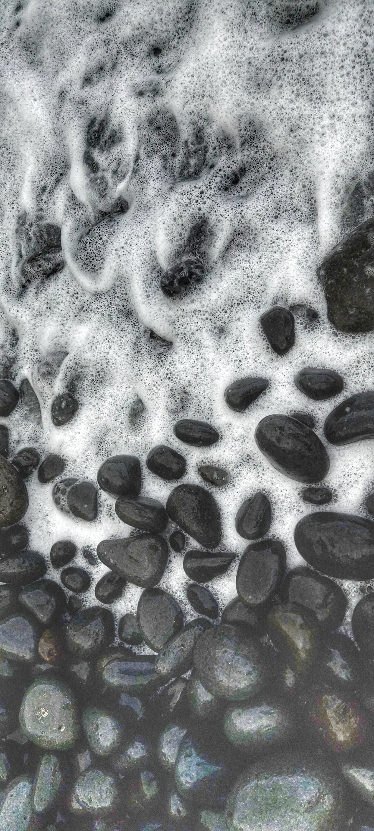 Round polished black rocks on a rocky beach with ocean foam in Mauritius