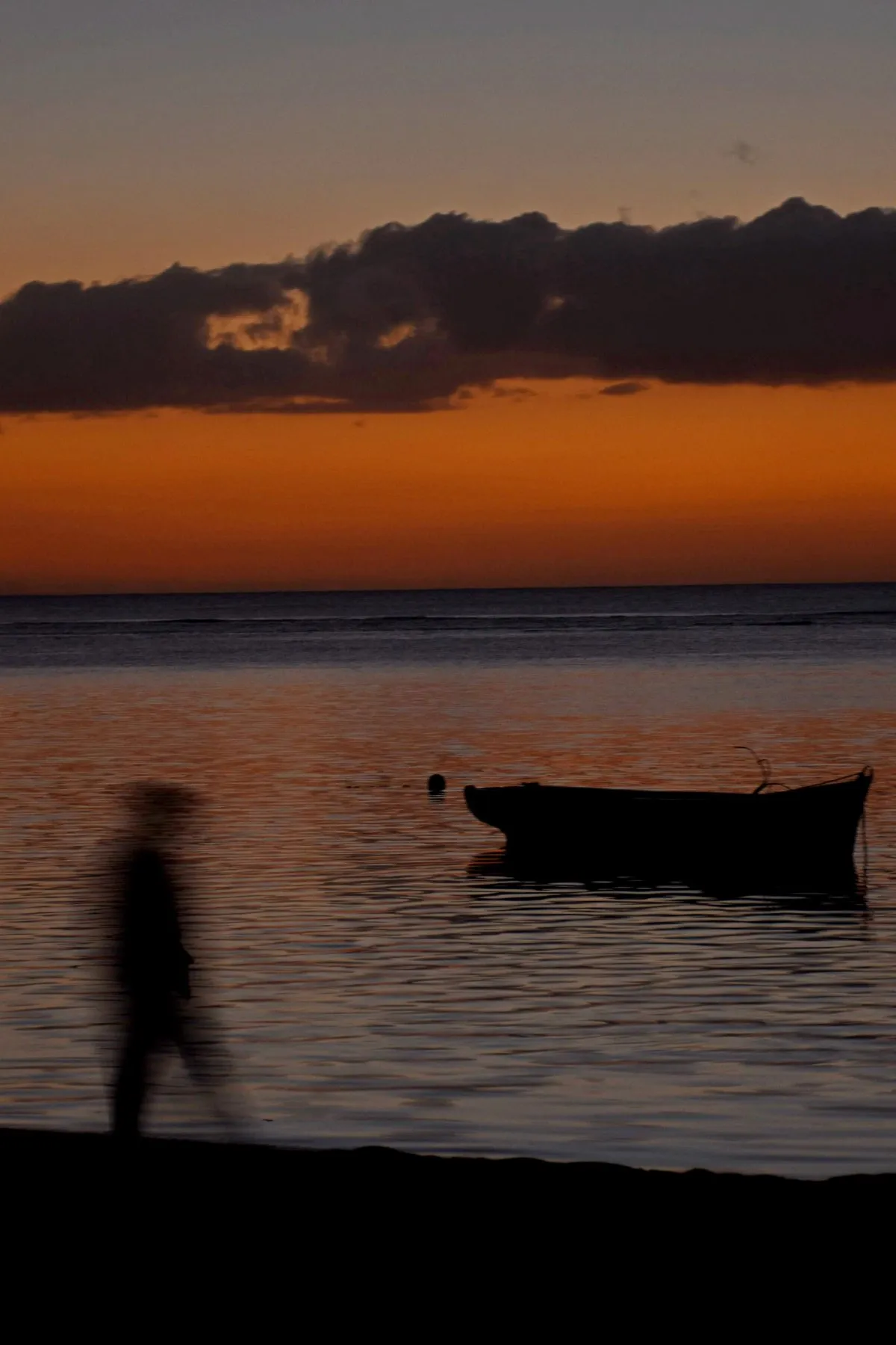 Silhouette of a man walking along Albion beach during sunset in Mauritius with long exposure effect