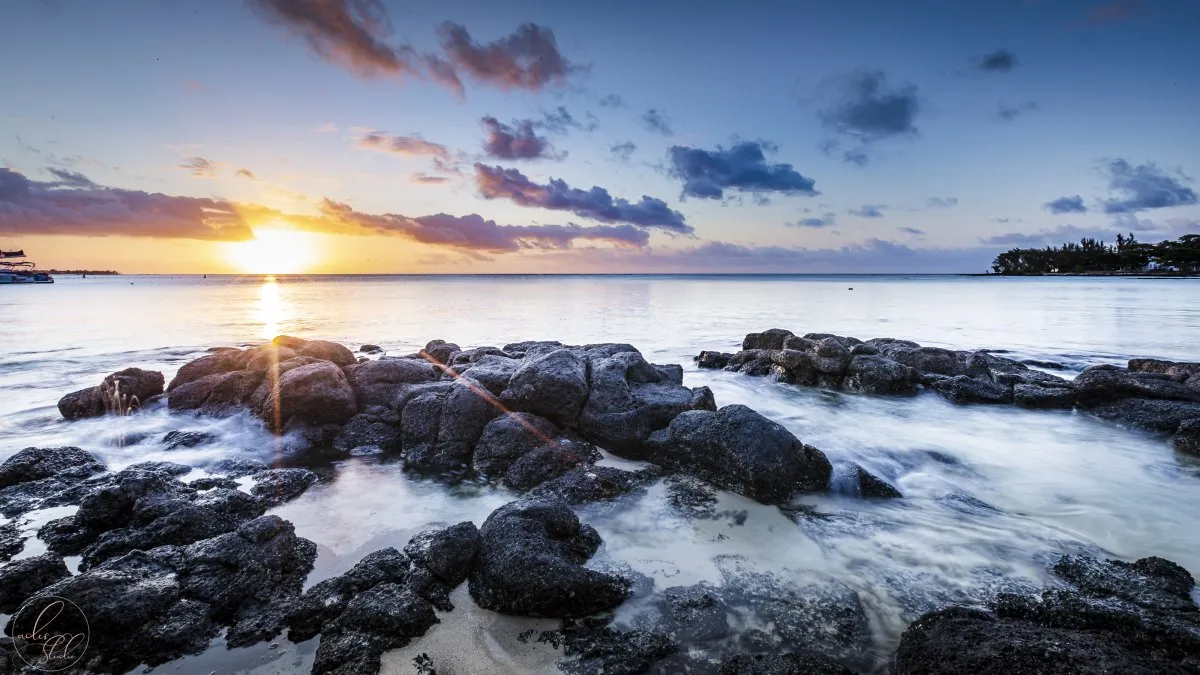 Sunset over the rocky shoreline at Pereybere with calm blue sea and sky in Mauritius