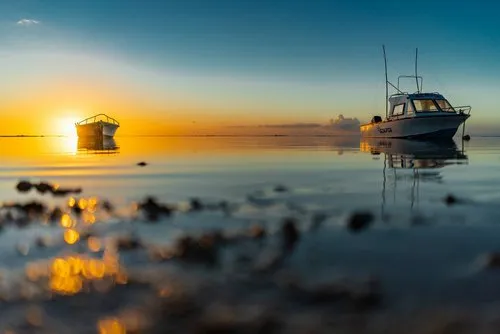 Boat partially hiding shy yellow sunset in the sea