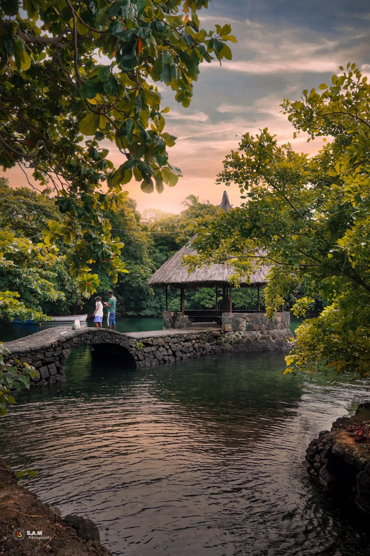 Stone jetty and estuary surrounded by forest at Trou d'eau douce in Mauritius with fishermen nearby