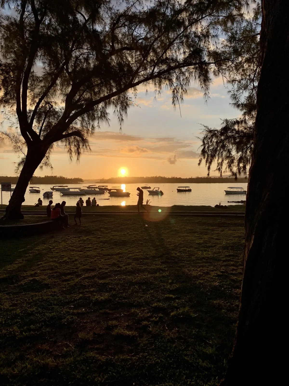 Sunset with sun flares over Blue Bay beach in Mauritius with people admiring the view