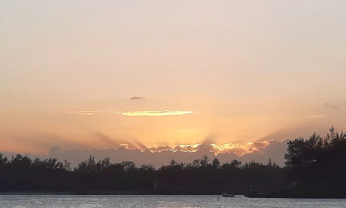 Sunset with sun rays behind clouds and tree silhouettes at Blue Bay Beach in Mauritius